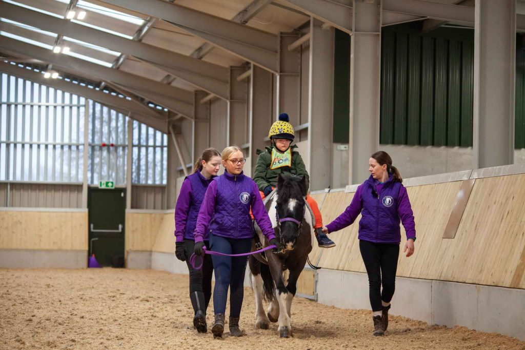 A rider being supported by three volunteers